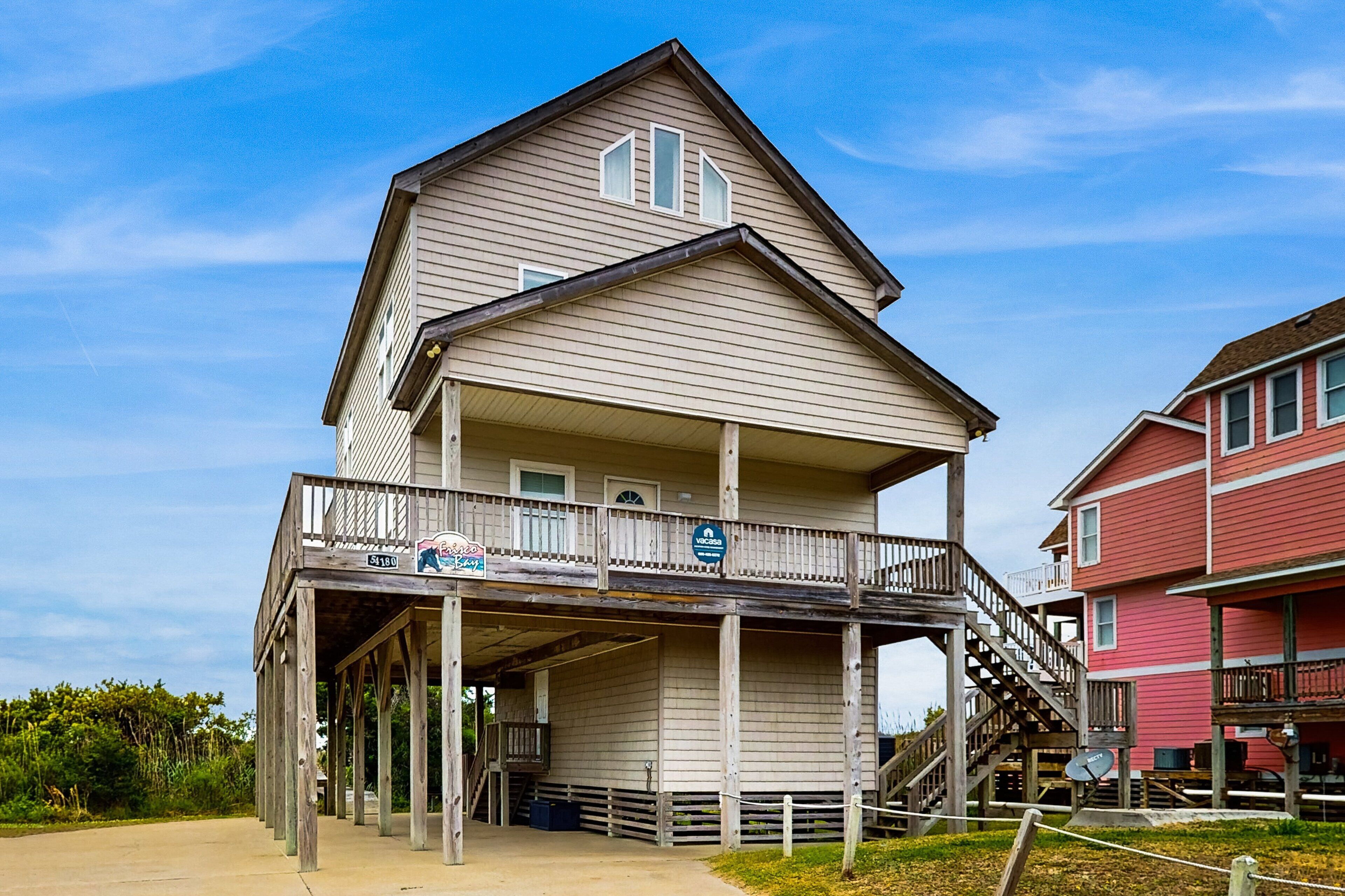 A two-story building with a balcony and a covered area, featuring a sign that reads "The Beach House."