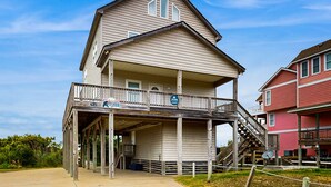 Kaksikerroksinen rakennus, jossa on parveke ja katettu alue. Rakennuksen edessä on kyltti, jossa lukee: ”The Beach House”.