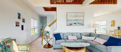 A spacious living room with a large sectional sofa, a coffee table, and a staircase leading to an upper level.