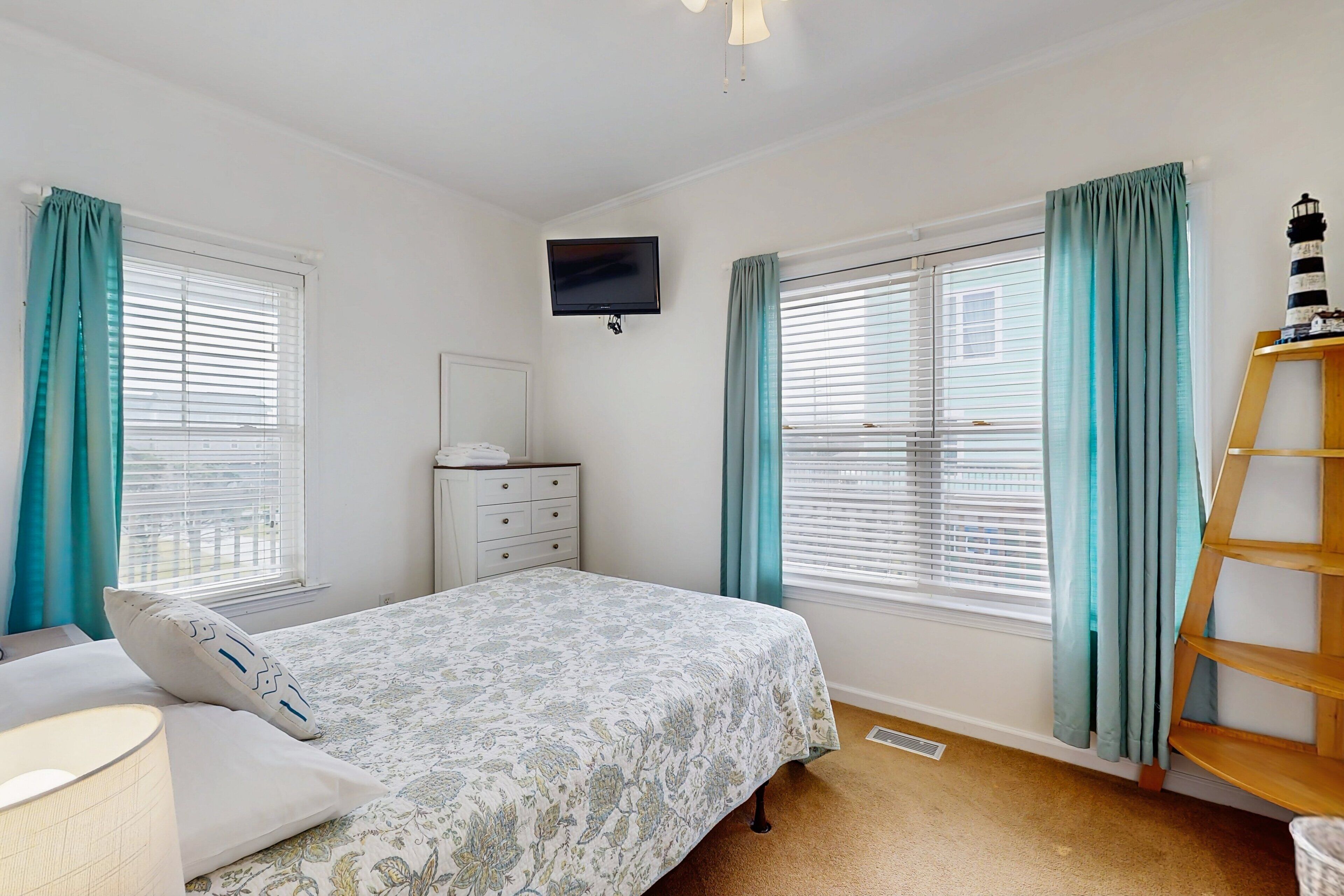A bedroom with a bed, a dresser, a TV mounted on the wall, and a window with curtains.