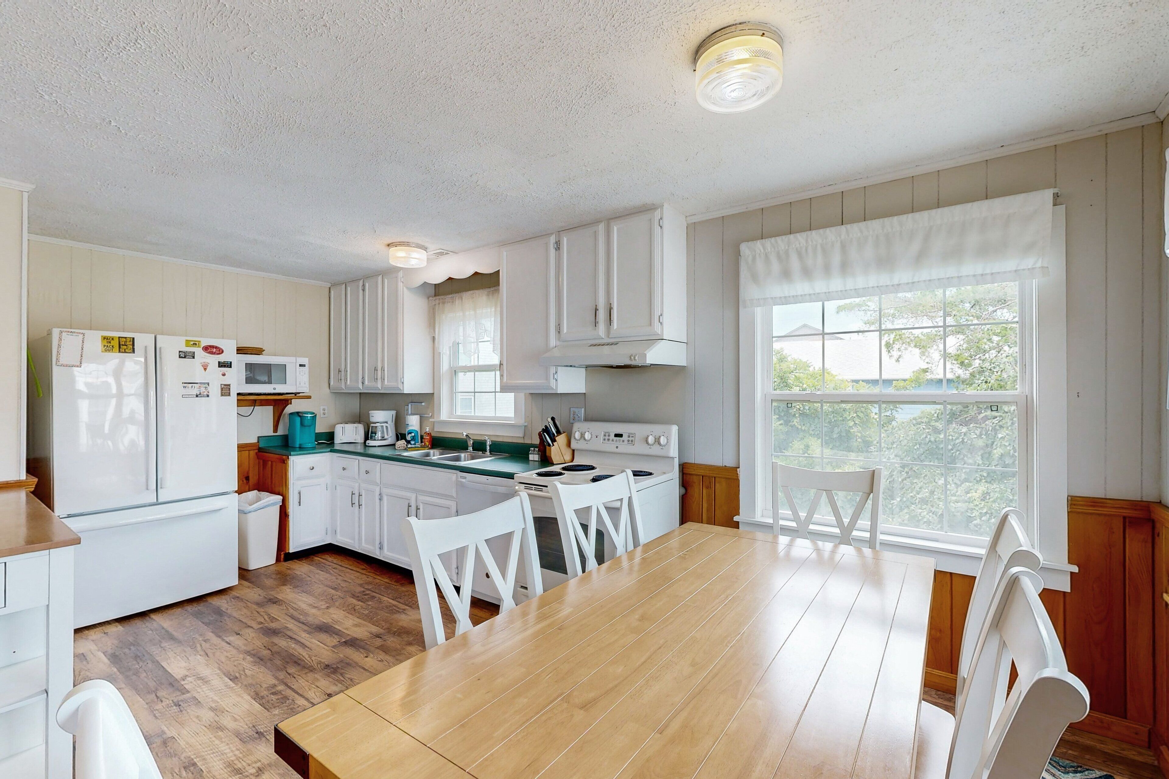 A kitchen with white cabinets, a wooden table, and a window with a view of trees.