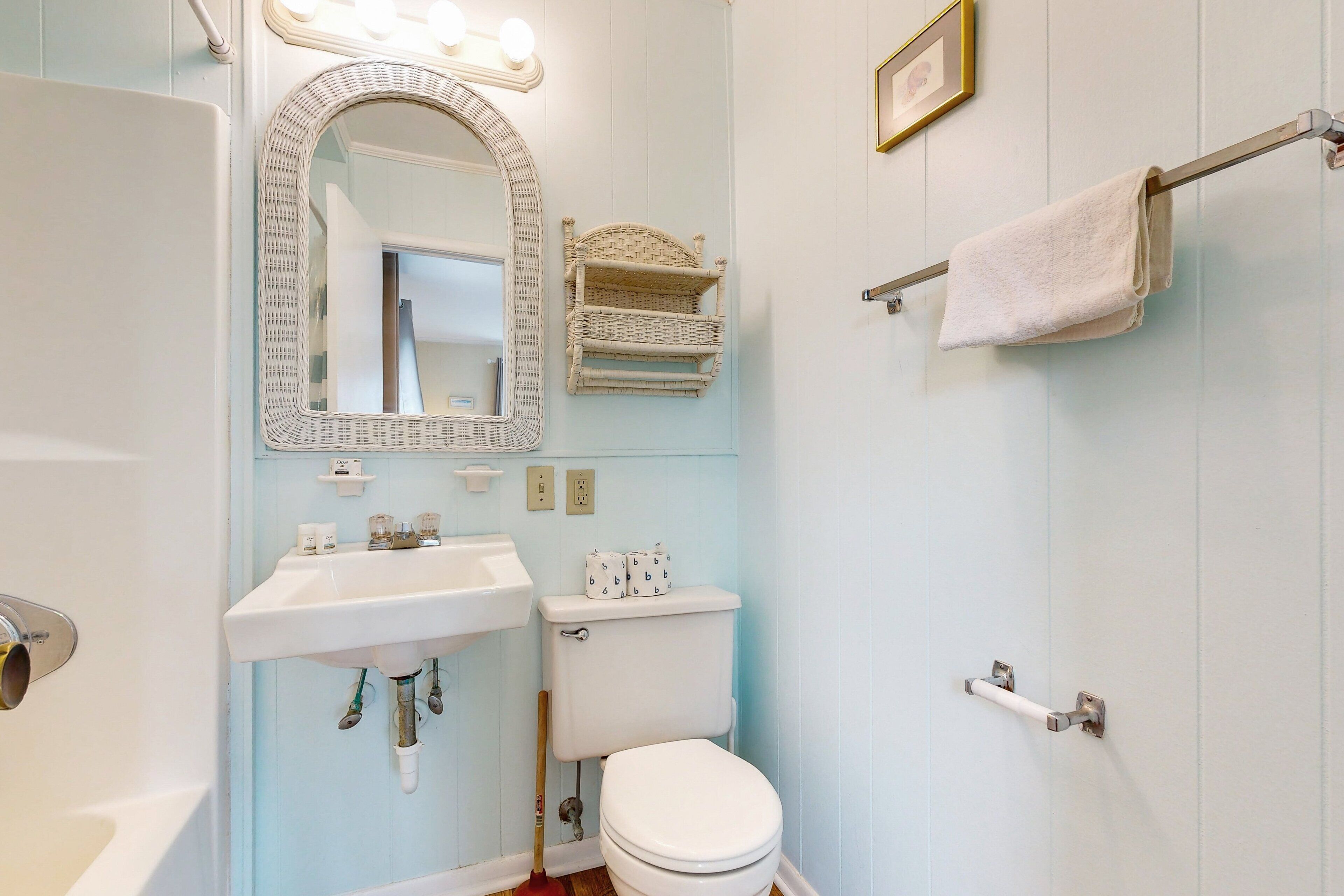 A bathroom with a white sink, toilet, and mirror. There are light switches and a towel rack on the wall.