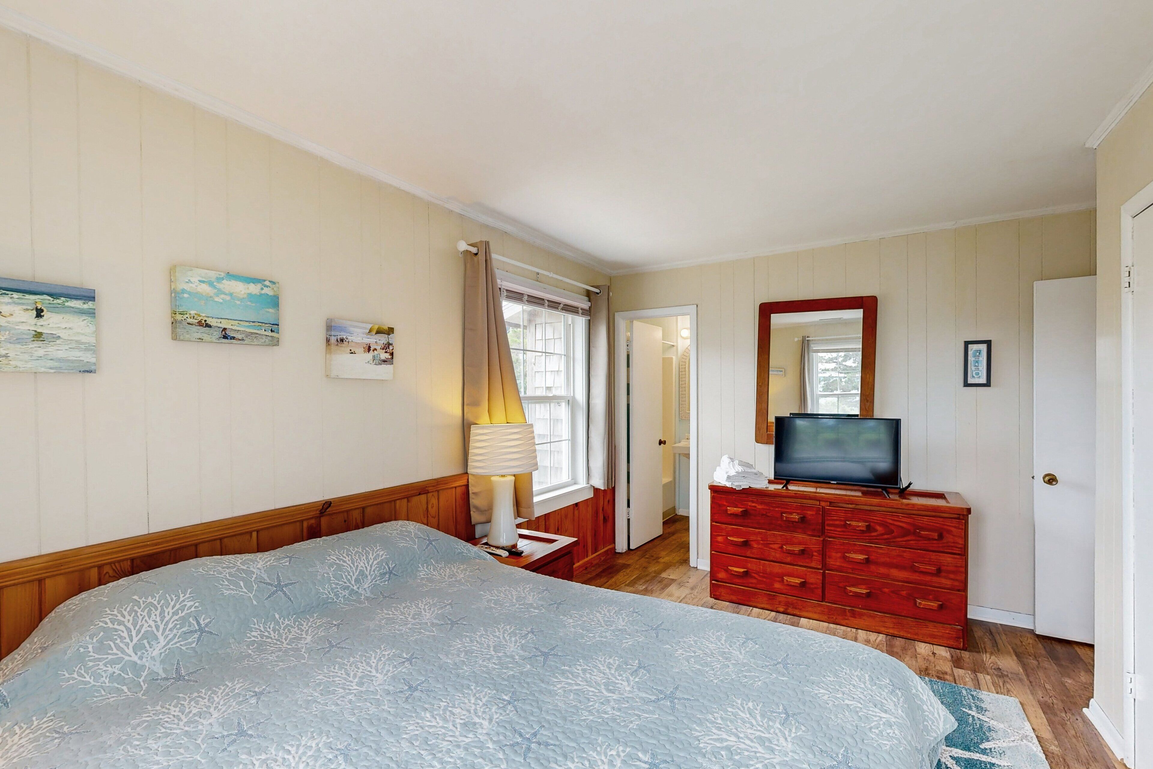 A bedroom with a bed, a dresser, a television, and wall art.