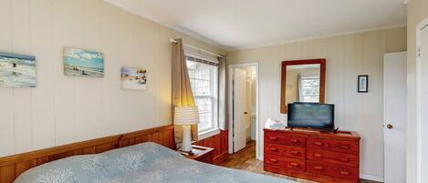 A bedroom with a bed, a dresser, a television, and wall art.