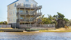 A multi-story waterfront building with balconies and a dock. - Stunning sound-front home with private hot tub, outdoor pool, & beach access (Rodanthe)