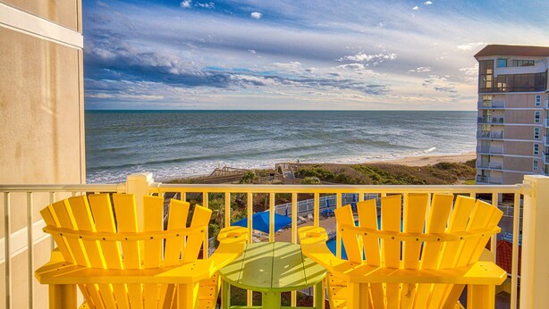 A balcony with yellow Adirondack chairs and a green table overlooking a beach and ocean. - St. Regis beachfront condo with ocean & pool-view balcony, gym & sauna (North Topsail Beach)
