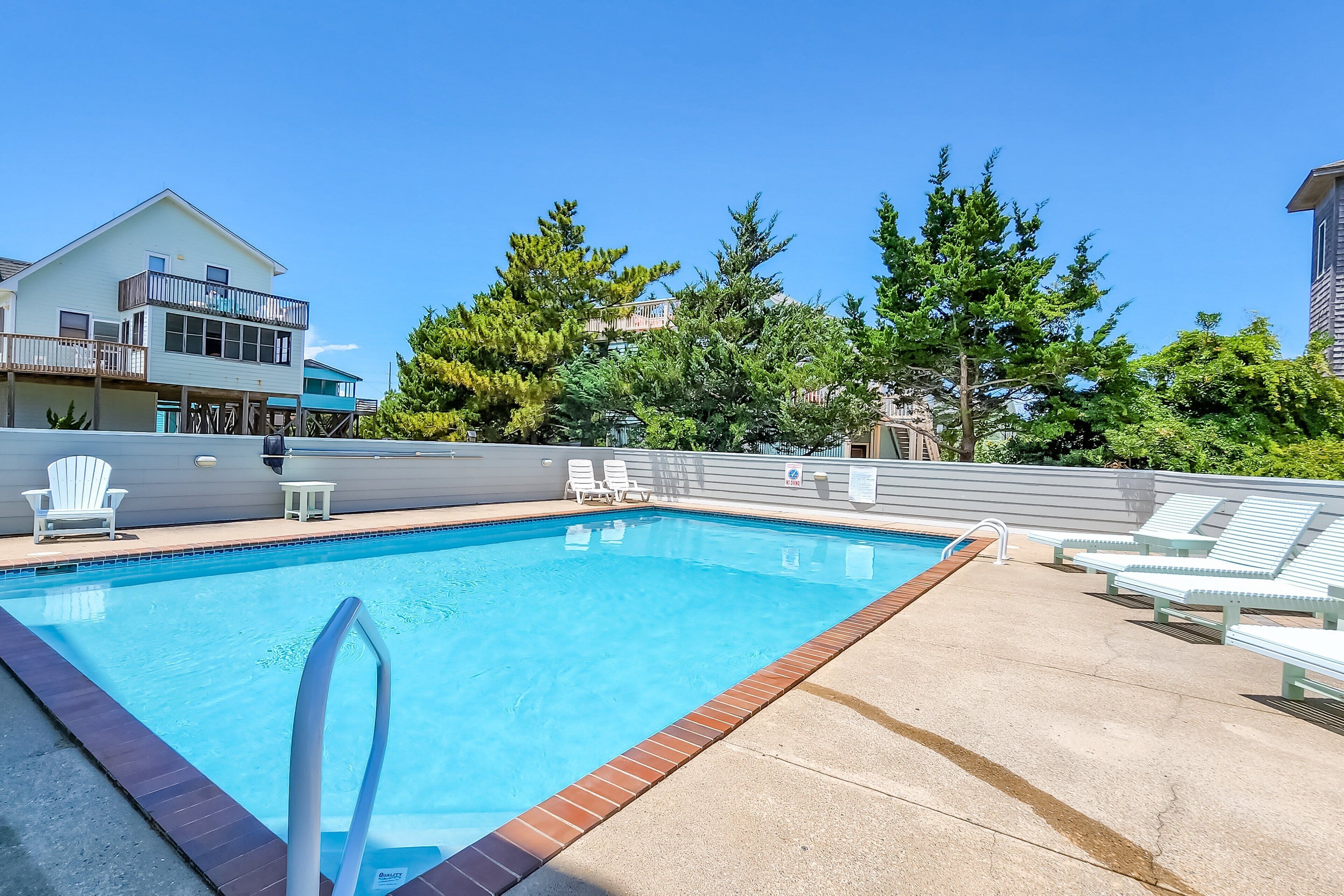A swimming pool with a clear blue water, surrounded by lounge chairs and a deck area.