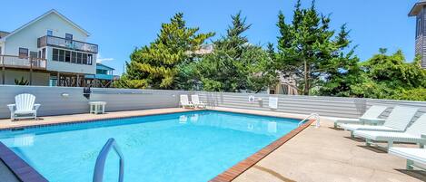 A swimming pool with a clear blue water, surrounded by lounge chairs and a deck area.