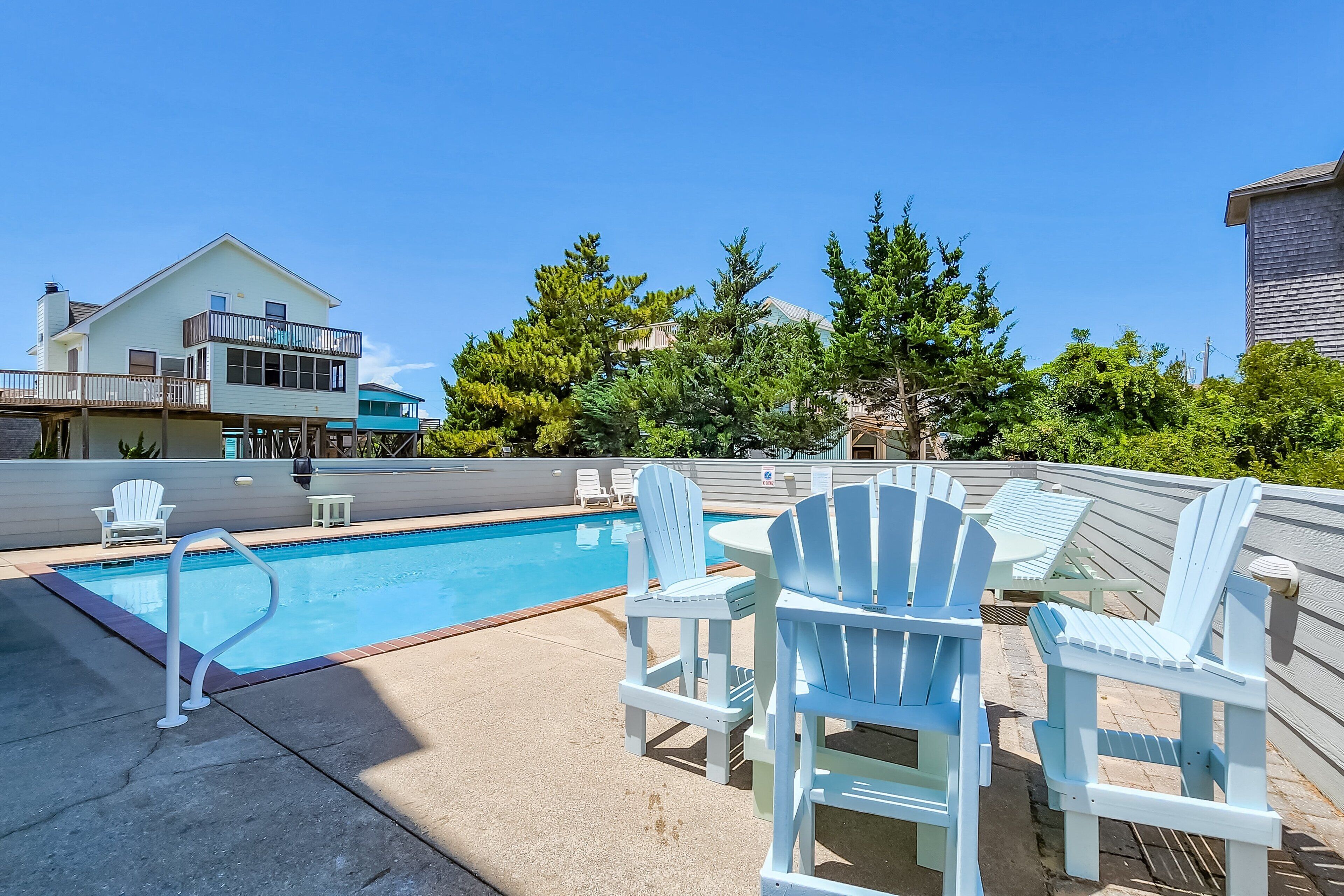 Une piscine entourée de chaises Adirondack et d’une terrasse.
