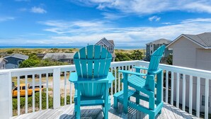 Un balcón con dos sillas Adirondack turquesas con vistas a la costa, donde se ven casas y un cielo despejado.