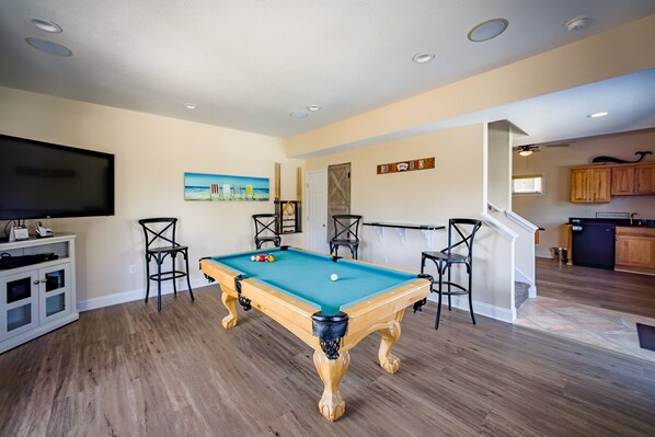 A pool table in a room with wooden flooring, a television, and a painting on the wall.