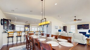 A spacious dining area with a long wooden table, multiple chairs, and a chandelier. - Oceanfront estate - heated pool, pool spa, elevator, pool table & cook's kitchen (North Topsail Beach)