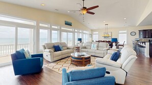 A spacious living room with a large window overlooking the ocean, a ceiling fan, and a dining area with a view. - Oceanfront estate - heated pool, pool spa, elevator, pool table & cook's kitchen (North Topsail Beach)