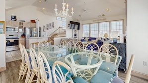 A spacious kitchen with a dining area, a TV mounted on the wall, and a staircase leading to another level. - Ocean-view home with private outdoor pool, hot tub, central AC, tennis & decks (Rodanthe)