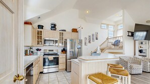 A spacious kitchen with modern appliances, a central island, and a staircase leading to a loft area. - Ocean-view home with private outdoor pool, hot tub, central AC, tennis & decks (Rodanthe)