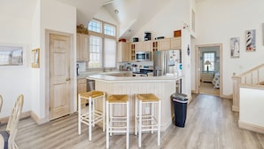 A spacious kitchen with a large island, wooden bar stools, and a view of the adjacent bedroom. - Ocean-view home with private outdoor pool, hot tub, central AC, tennis & decks (Rodanthe)