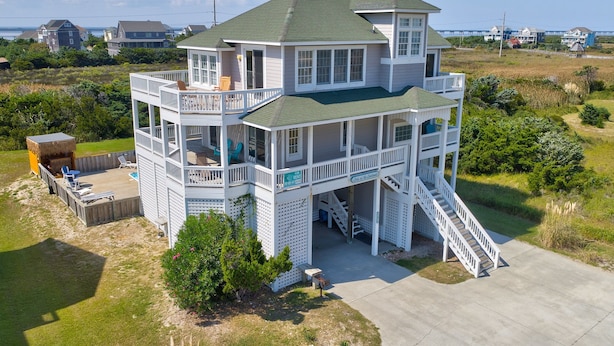 A two-story beachfront house with multiple balconies, a covered deck, and a staircase leading to the upper level. - Ocean-view home with private outdoor pool, hot tub, central AC, tennis & decks (Rodanthe)