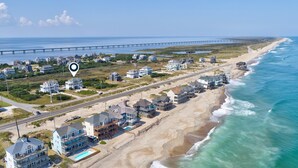 An aerial view of a coastal residential area with houses, a beach, and a pier in the background. - Ocean-view home with private outdoor pool, hot tub, central AC, tennis & decks (Rodanthe)