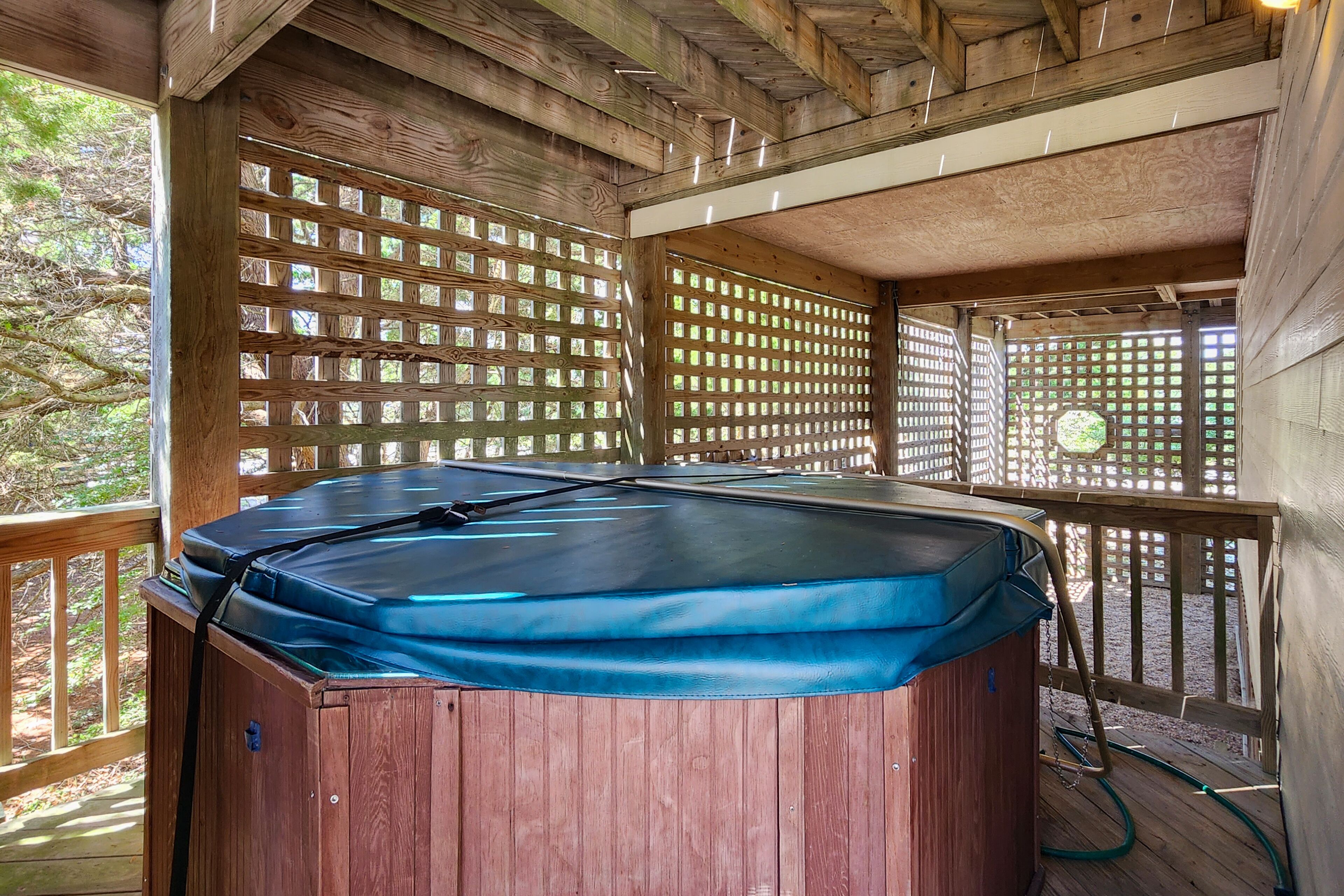 A hot tub in a wooden deck area with a wooden lattice wall and a view of trees.