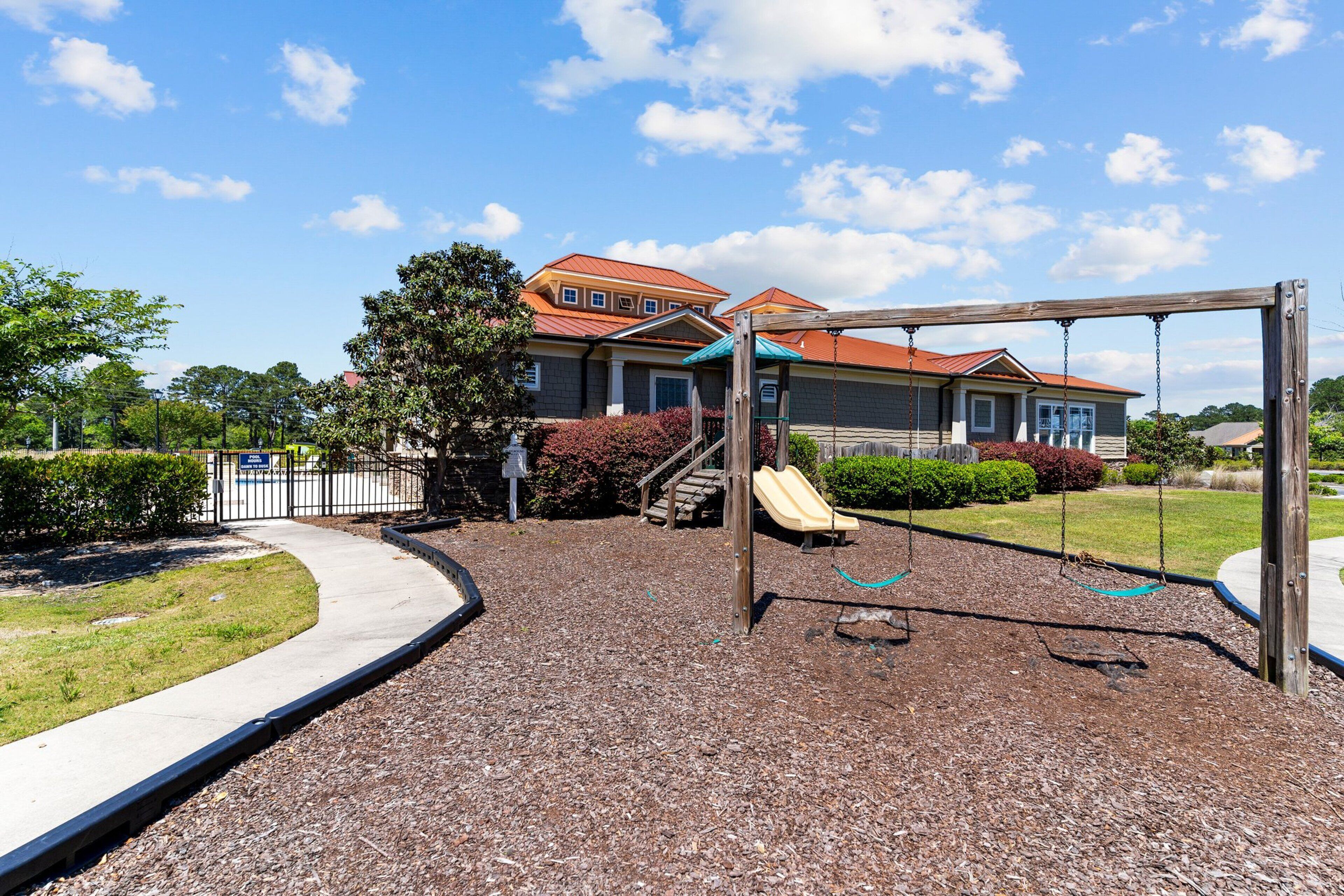 A playground with a slide and swings, surrounded by a landscaped area with mulch and trees.