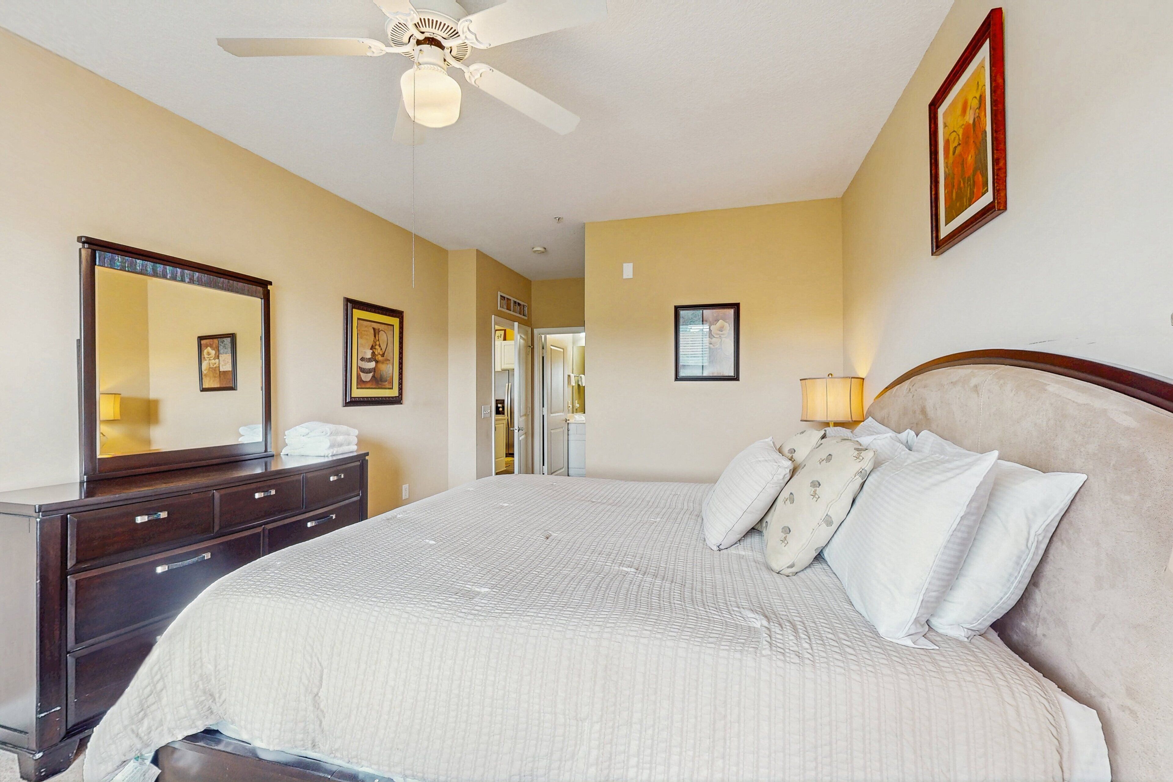Een hotelkamer met een bed, een dressoir, een plafondventilator en een schilderij aan de muur.