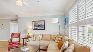Una sala de estar con un sofá beige, una mesa de centro de madera, un sillón rojo y un cuadro con una vista urbana en la pared.