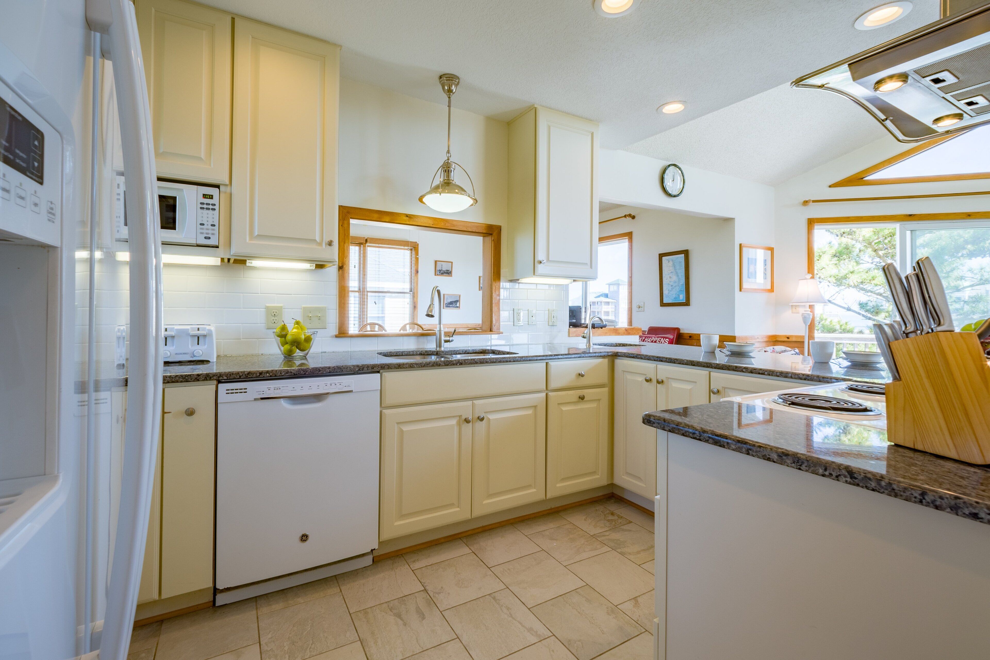 A modern kitchen with white cabinets, a granite countertop, a dishwasher, a microwave, and a sink.