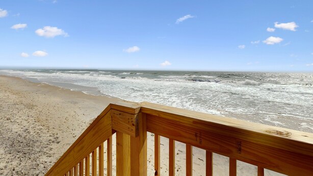 Une terrasse en bois donnant sur une plage où l’on peut admirer les vagues.
