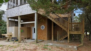 A wooden house with a covered porch, a staircase, and a small outdoor seating area. - Dog-friendly house short walk from beach with pool table & WiFi (Frisco)
