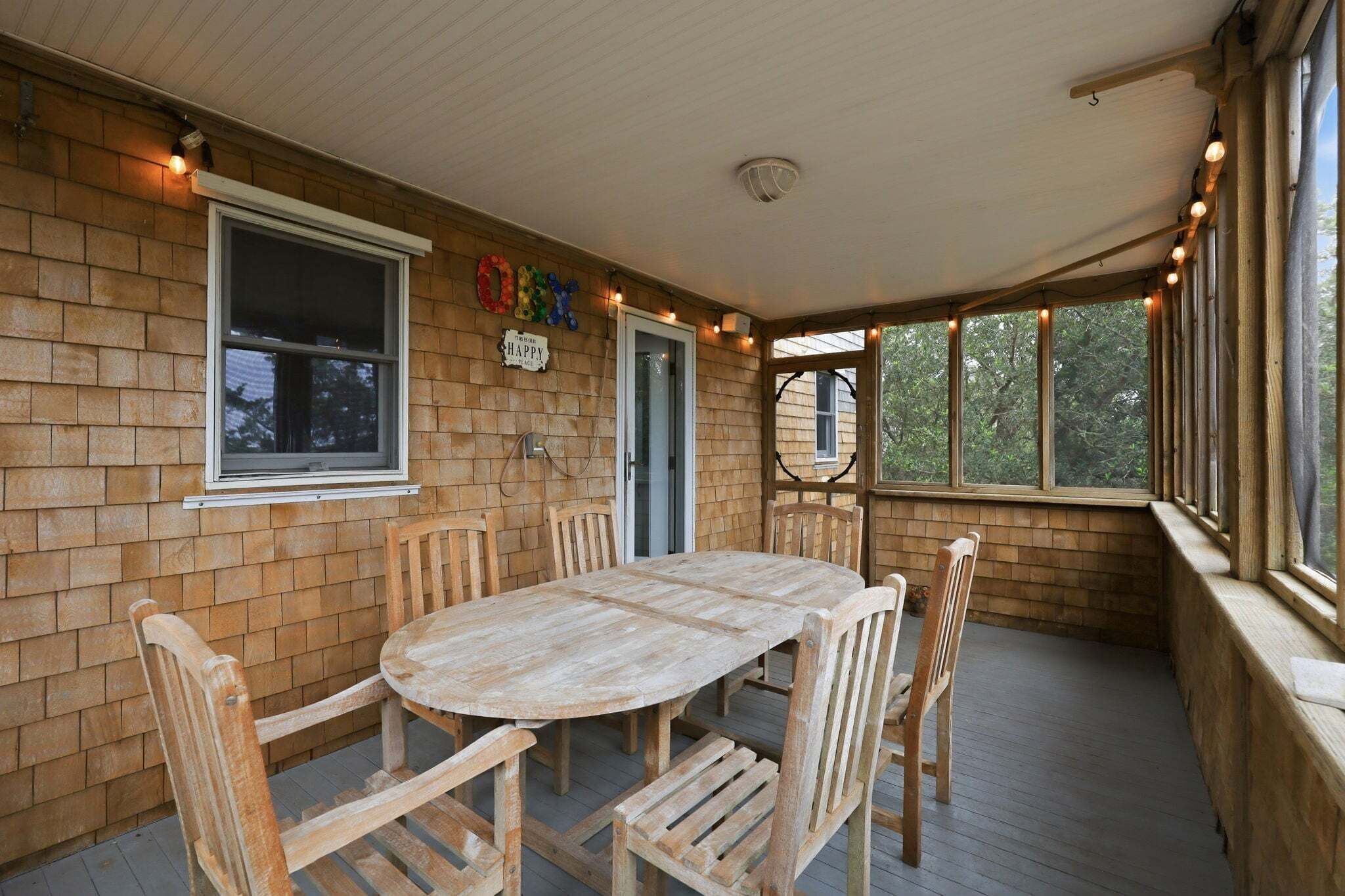 A covered patio with a wooden table and chairs, brick walls, and windows.