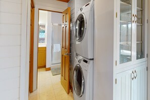 A laundry room with two stacked front-loading washing machines, a wooden door, and a cabinet with glass doors.