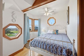 A bedroom with a bed, a ceiling fan, a window with a view, and a decorative octagonal mirror. - Dog-friendly house short walk from beach with pool table & WiFi (Frisco)
