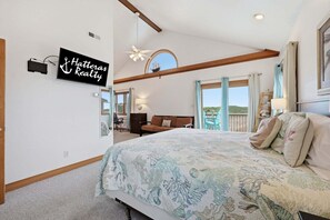 A bedroom with a bed, a desk, a chair, and a view of the outdoors.