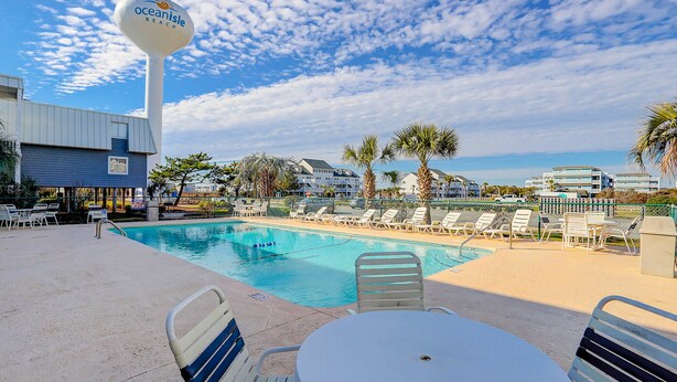 A pool area with lounge chairs and a sign for Ocean Isle Beach. - Sandvillas C1: 2nd-Floor | Balcony | Pool (Ocean Isle Beach)