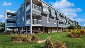 A multi-story residential building with balconies, a covered outdoor area, and a well-maintained lawn. - Sandvillas C1: 2nd-Floor | Balcony | Pool (Ocean Isle Beach)