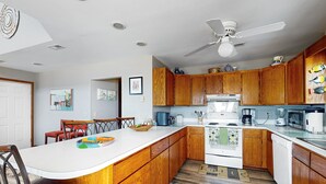 Une cuisine moderne avec des meubles en bois, un plan de travail blanc et un ventilateur de plafond.