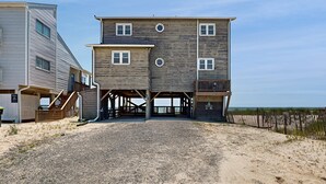 Un bâtiment en bois à deux étages, doté d’un balcon et d’un escalier, avec une plage de sable en arrière-plan.