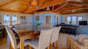 A spacious living area with a wooden ceiling, a dining table with chairs, a sofa, and a television. - Luxe ocean-view beach estate - amazing views, private pool, hot tub & elevator (North Topsail Beach)