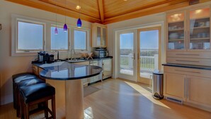 A modern kitchen with a central island, wooden ceiling, and large windows. - Luxe ocean-view beach estate - amazing views, private pool, hot tub & elevator (North Topsail Beach)