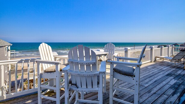 A wooden deck with white Adirondack chairs and a table overlooking the ocean. - Luxe ocean-view beach estate - amazing views, private pool, hot tub & elevator (North Topsail Beach)
