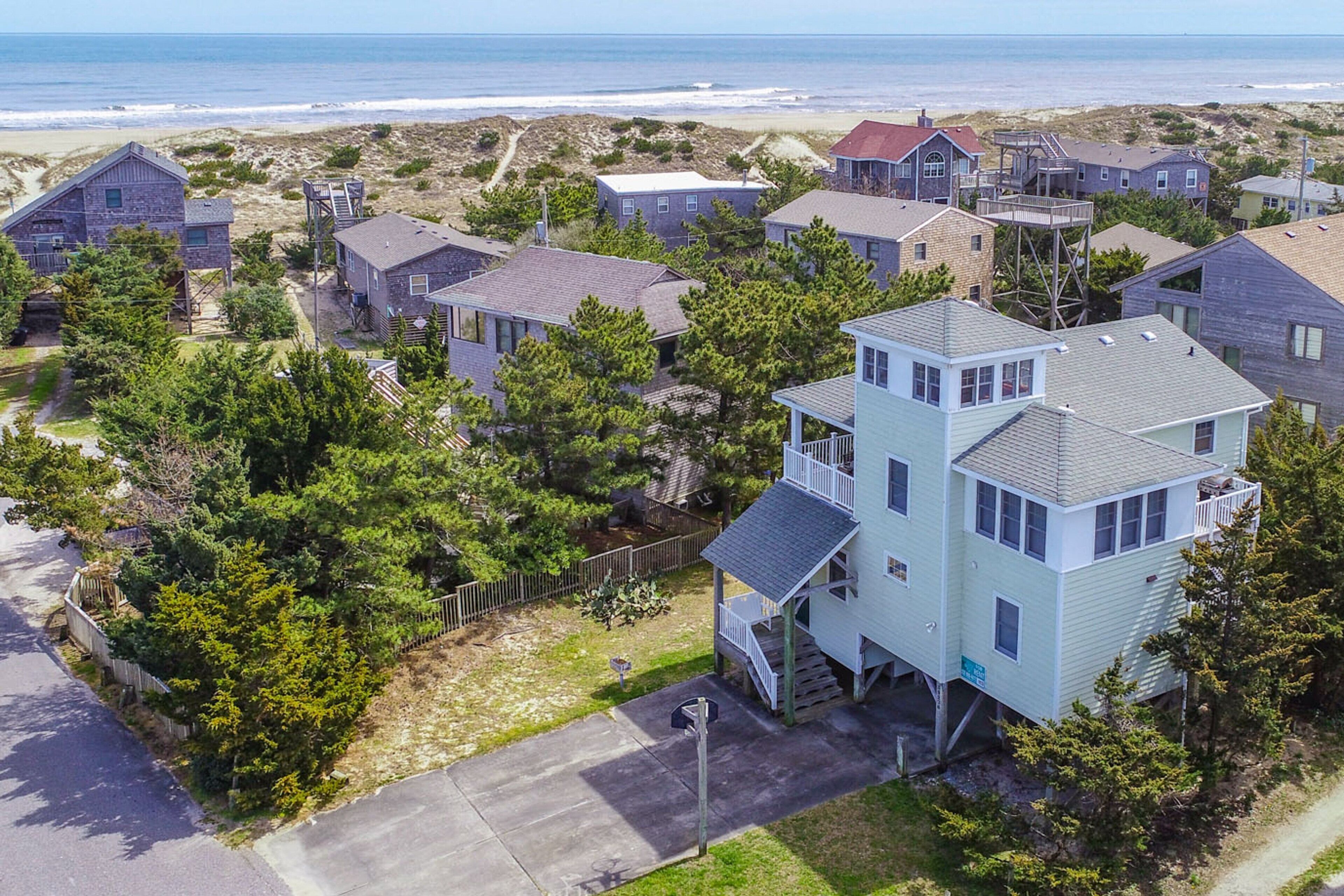 A coastal residential area with houses, including a two-story house with a balcony and a view of the ocean.