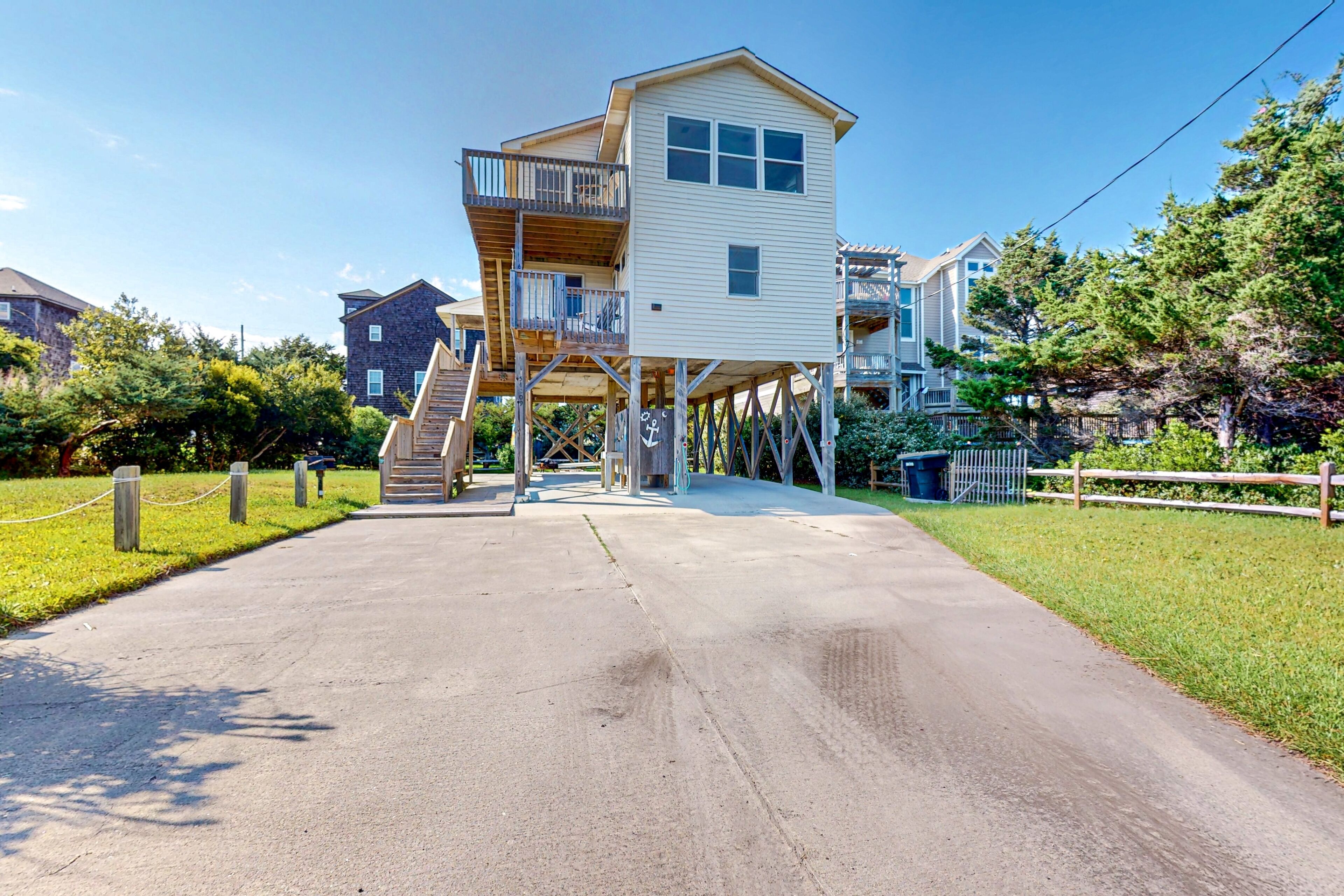 A two-story wooden house with a balcony on the upper floor, a concrete driveway, and a fenced yard.