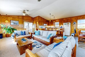A cozy cabin-style room with wooden walls, a sofa, a dining table, and a kitchen area with a refrigerator and microwave.