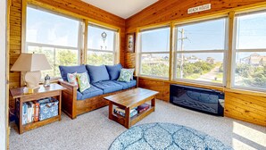 Ein gemütliches Blockhäuschen-Interieur mit einem blauen Sofa, Holzwänden, großen Fenstern und einem Kamin.