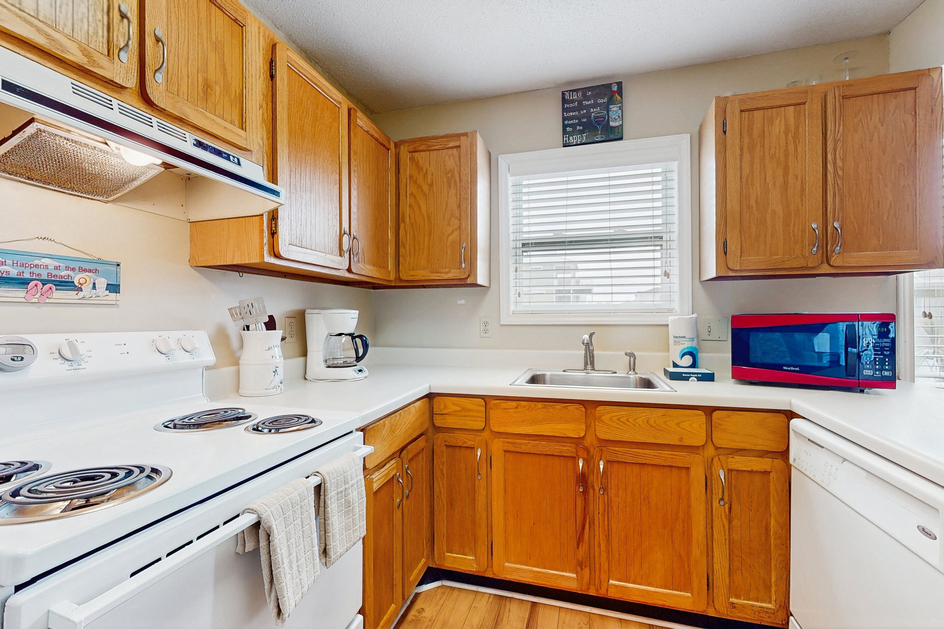 A kitchen with wooden cabinets, a white stove, a microwave, and a sink.