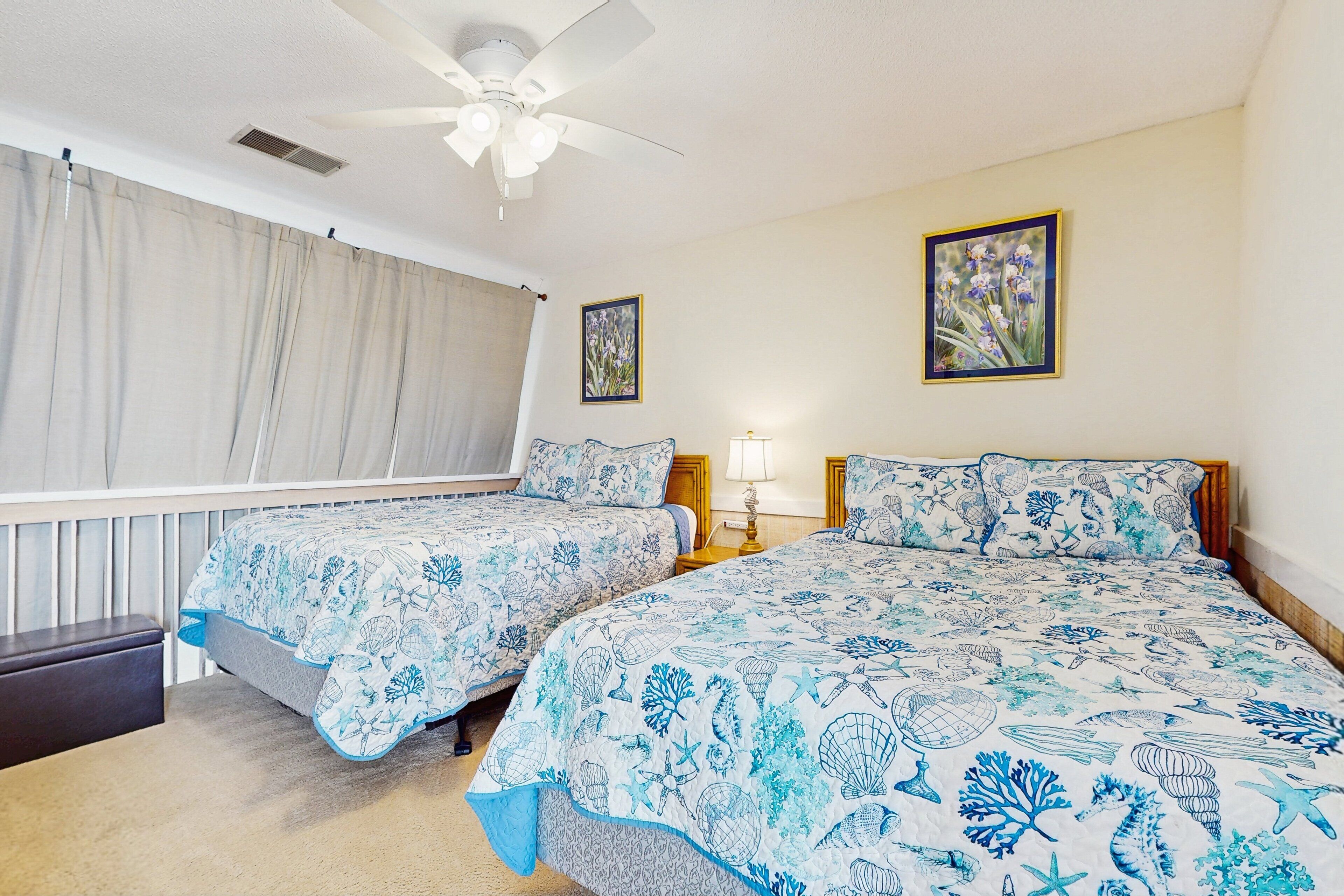 A bedroom with two beds, a ceiling fan, and a window with curtains.