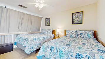 A bedroom with two beds, a ceiling fan, and a window with curtains.