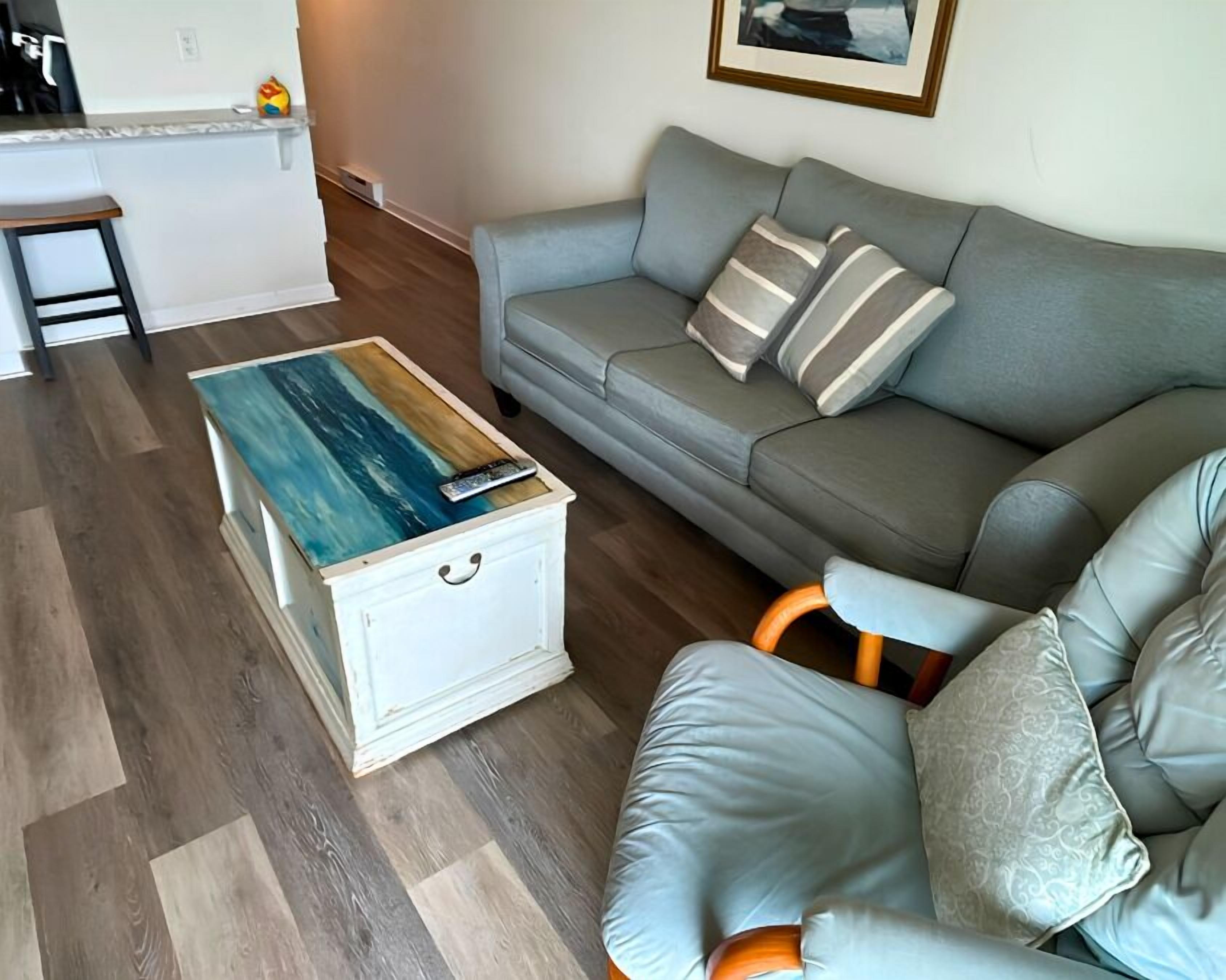 A living room with a grey sofa, a white coffee table with a painted top, and a cushioned chair.