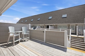 Une terrasse en bois avec des chaises, un escalier et un bâtiment doté de nombreuses fenêtres.