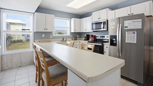 Une cuisine moderne dotée d’un îlot central, de meubles blancs, d’appareils électroménagers en acier inoxydable et offrant une vue sur l’extérieur.
